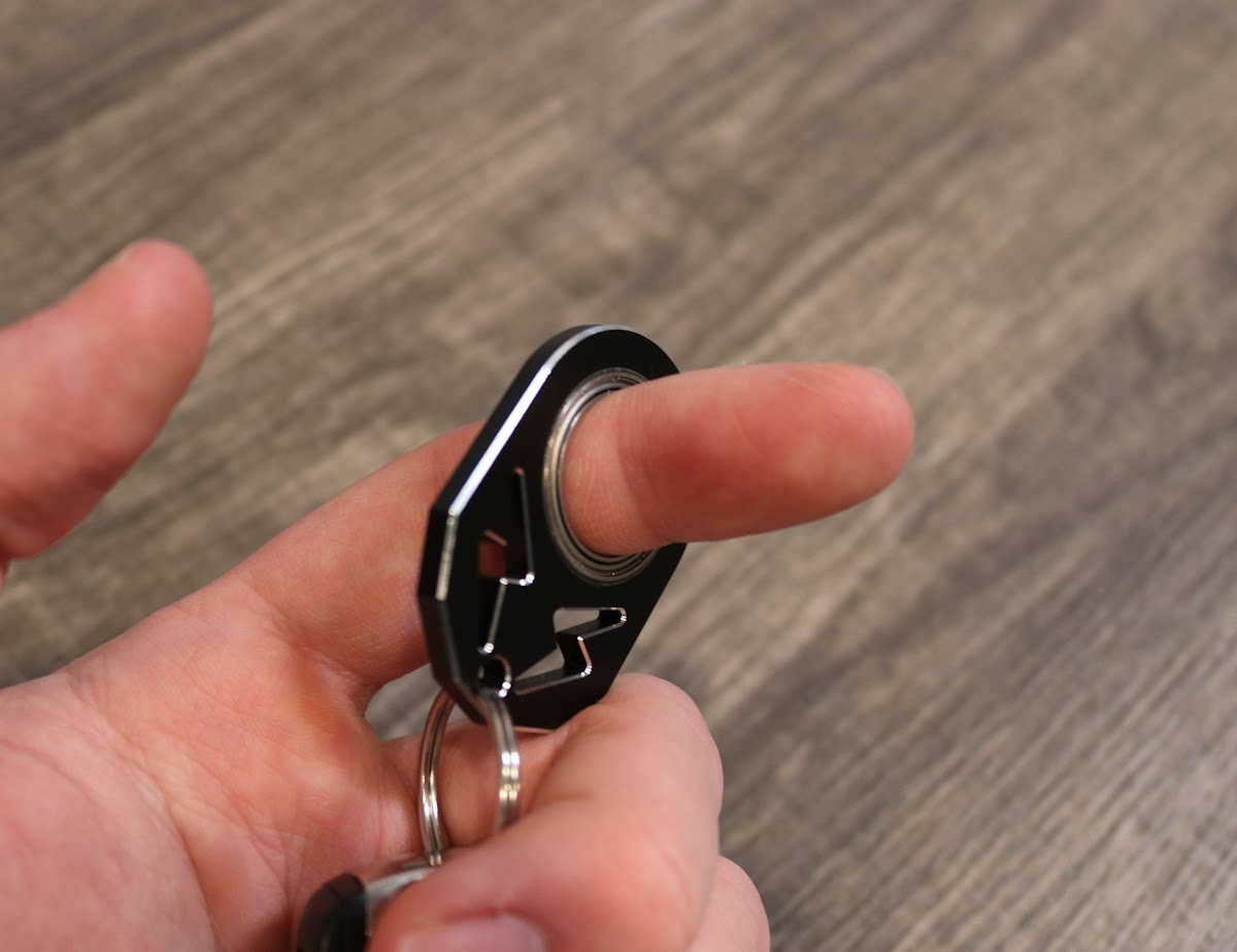 Person holding the KeyKaram key spinner between their fingers, demonstrating the ergonomic grip and keyring attachment